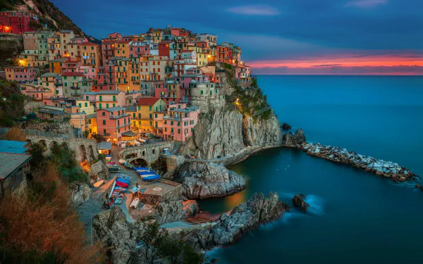 Sunset over the vibrant, colorful cliffside village of Manarola, Italy, captured in an HD desktop wallpaper showcasing the calm sea and dramatic sky.