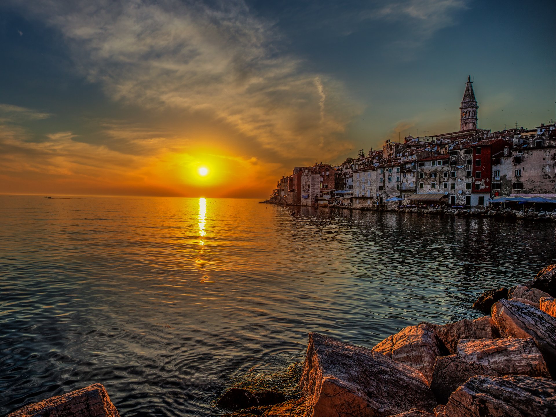 Sunset over the coastal town of Rovinj, Croatia, showcasing historic buildings along the shoreline with a calm sea and vibrant orange sky in 4K Ultra HD.