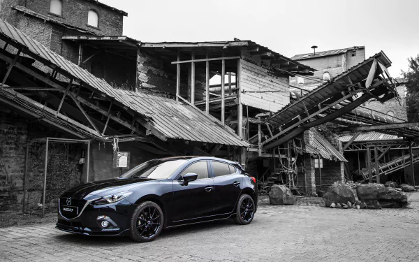 Black Mazda 3 hatchback vehicle parked in front of a dilapidated industrial building — 4K Ultra HD desktop wallpaper background.
