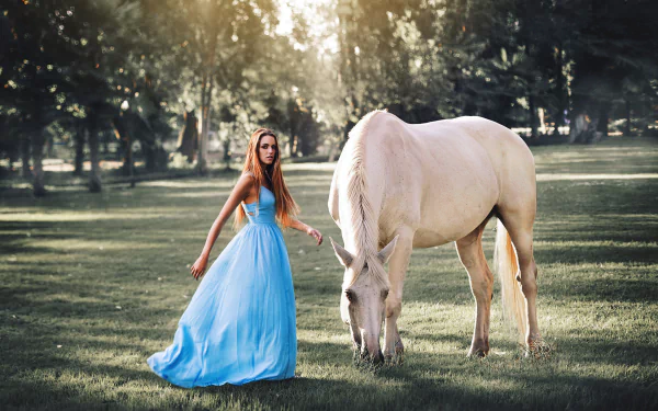 A brunette woman in a blue dress stands beside a white horse in a sunny, bokeh-filled outdoor setting. This HD wallpaper exudes a serene, natural ambiance.