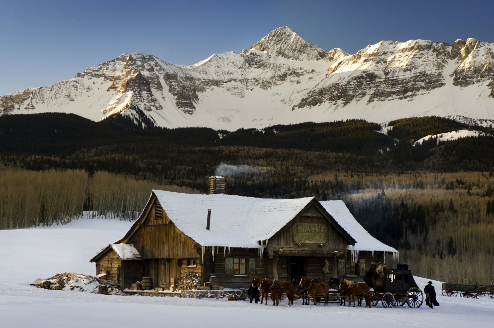 HD desktop wallpaper featuring a snowy mountain landscape and rustic cabin from the movie The Hateful Eight.