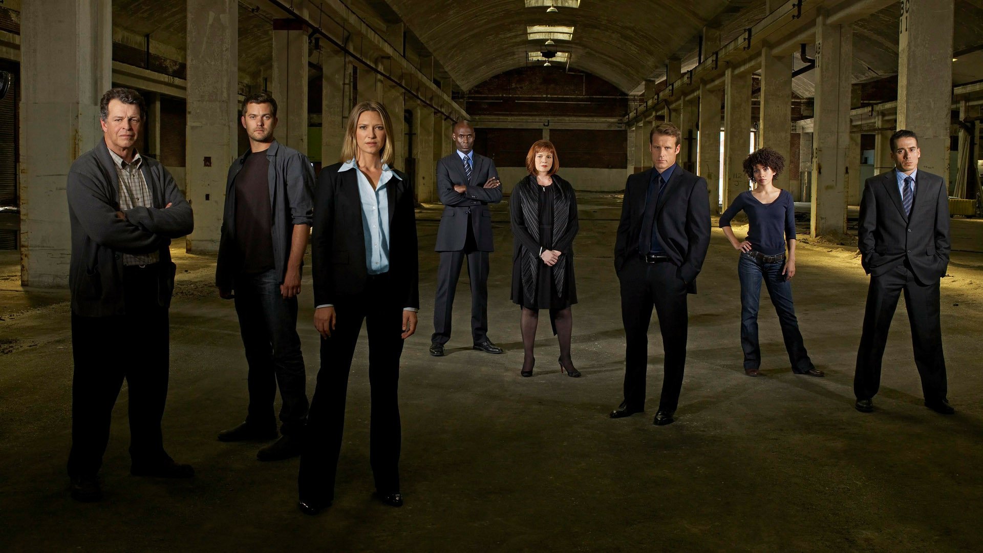 HD PC desktop wallpaper featuring the main cast of the TV show Fringe standing in a dimly lit, abandoned industrial space.