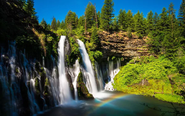 HD PC desktop wallpaper: Burney Falls cascading through green trees with a rainbow arcing over the emerald pool, vibrant nature background.