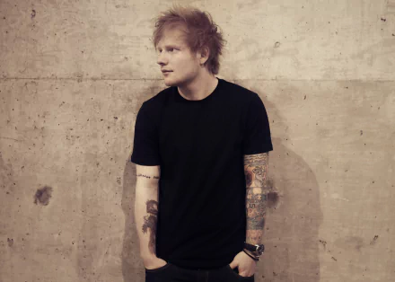 HD desktop wallpaper of an English singer with tattoos, standing against a concrete wall.