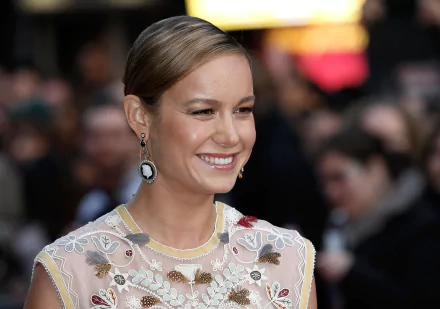 Brie Larson, American actress with brunette hair, brown eyes, and elegant earrings, smiles brightly in this HD PC desktop wallpaper and background.