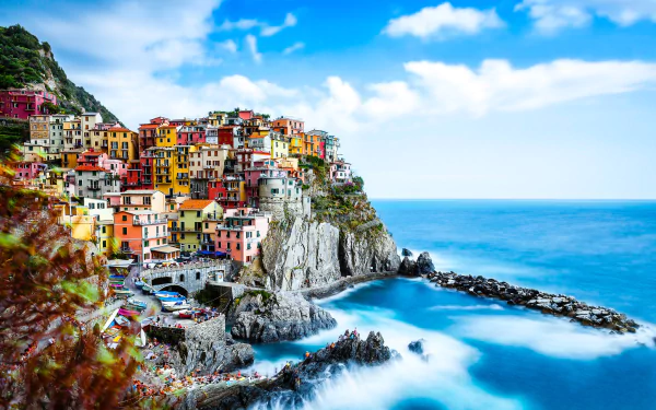 Colorful man-made village of Manarola perched on the rugged Italian coast, overlooking the vibrant ocean under a bright blue sky in HDR quality.