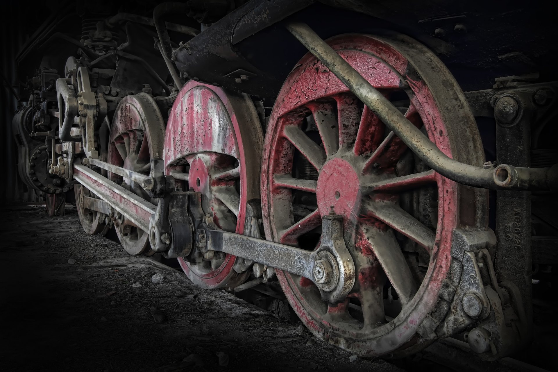 Close-up of aged red locomotive driving wheels and connecting rods, textured with rust and grime; 4K Ultra HD PC desktop wallpaper background.