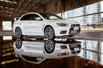 A sleek white Mitsubishi Lancer Evolution is showcased, reflecting beautifully on a wet surface inside an industrial setting, surrounded by modern architecture.
