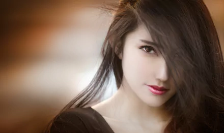 Wallpaper featuring an Asian brunette model with brown eyes and lipstick, gazing intently with soft lighting in the background.