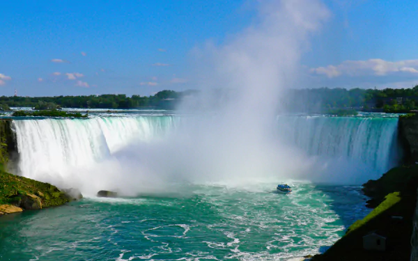 4K Ultra HD desktop wallpaper of Niagara Falls showcasing powerful cascading water, mist rising, and lush greenery under a bright blue sky.