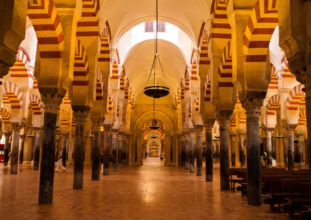 A stunning view of the interior of the Mosque-Cathedral in Córdoba, Spain, showcasing its iconic arches and striped columns in a warm, inviting atmosphere.
