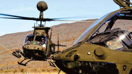 HD desktop wallpaper featuring two military Bell OH-58 Kiowa helicopters flying over a desert landscape under a clear blue sky.