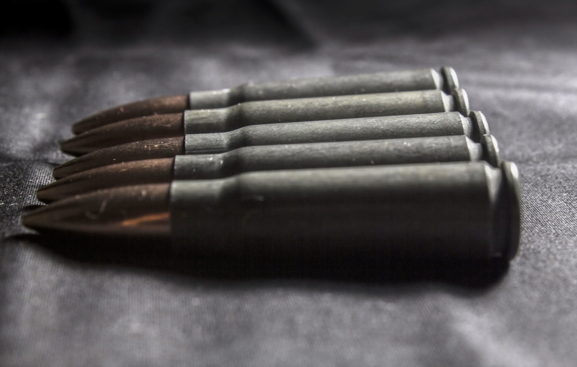 Close-up of man-made rifle bullets lined on a dark surface, HD PC desktop wallpaper/background.