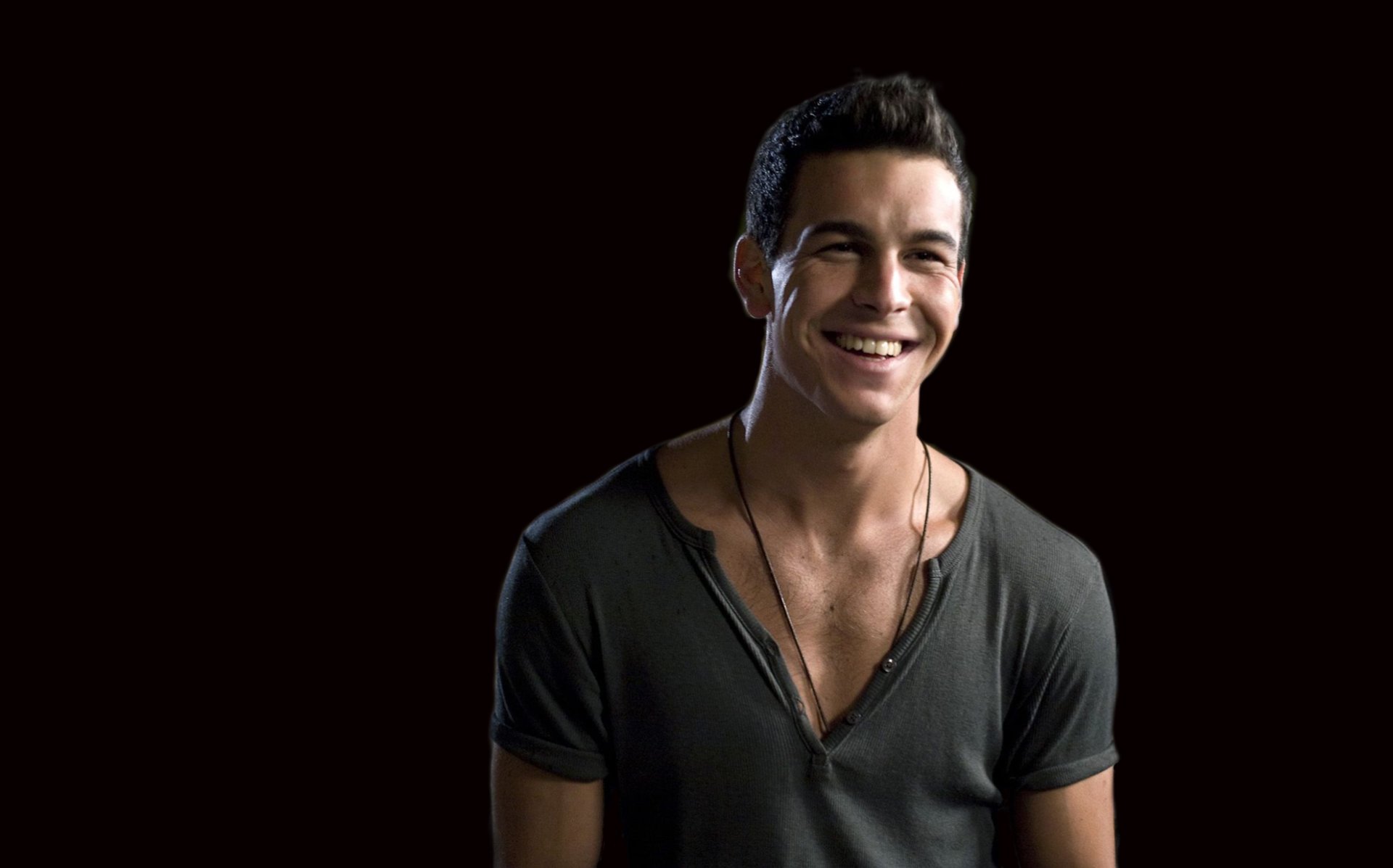 HD PC desktop wallpaper: smiling man in a deep V-neck shirt against a dark background, casual pose with a warm, confident expression.