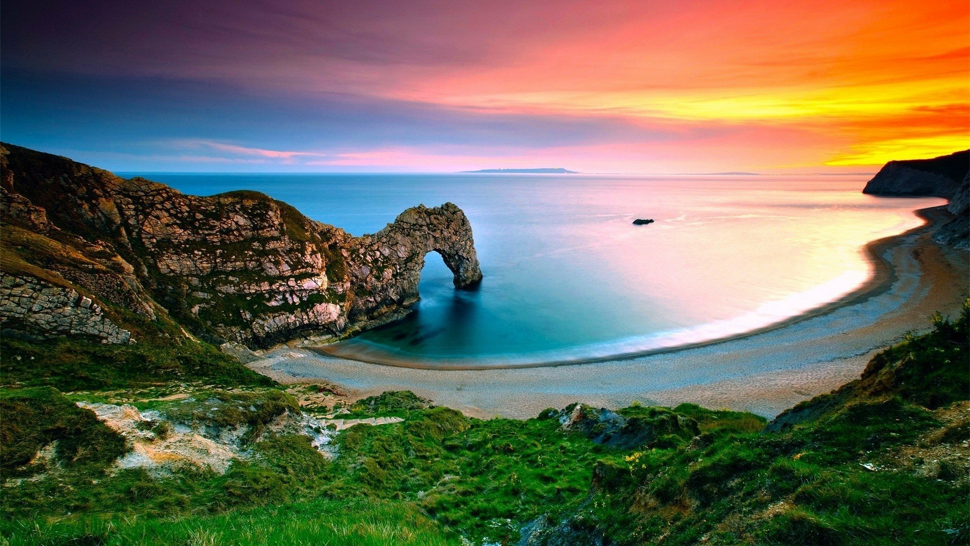 Sunset over Durdle Door on the Dorset coastline: curved beach, ocean horizon and green cliffs — HD PC desktop wallpaper showcasing England's coastal nature.