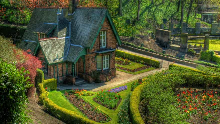 A charming cottage nestled in a vibrant garden in England, showcasing beautifully manicured flowerbeds and lush greenery, captured in stunning HDR for a captivating desktop background.