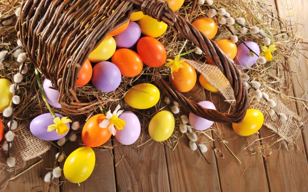 A 4K Ultra HD desktop wallpaper featuring colorful Easter eggs spilling from a woven basket onto a wooden surface, accented with daffodils and spring holiday decor.