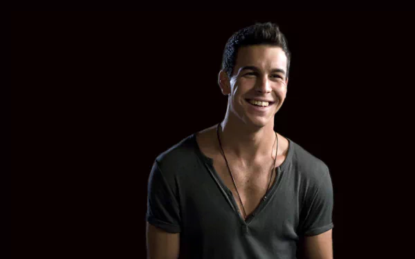 HD PC desktop wallpaper: smiling man in a deep V-neck shirt against a dark background, casual pose with a warm, confident expression.