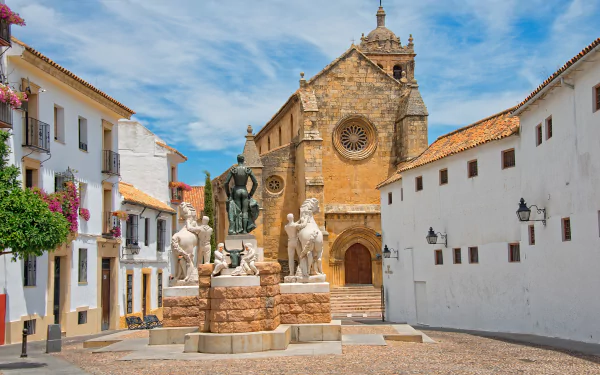 HD desktop wallpaper of a Córdoba, Spain plaza with a historic church façade and a central man-made fountain statue framed by whitewashed buildings.