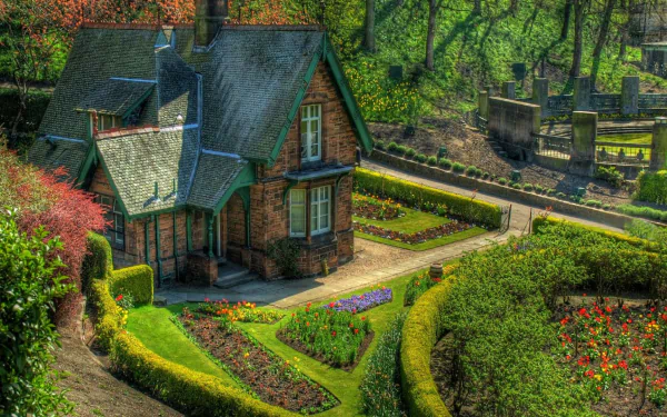 A charming cottage nestled in a vibrant garden in England, showcasing beautifully manicured flowerbeds and lush greenery, captured in stunning HDR for a captivating desktop background.
