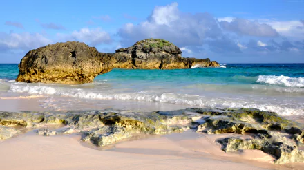 A vibrant 4K Ultra HD wallpaper of Bermuda’s beach, showcasing rocky shorelines, turquoise ocean waves, and a clear horizon under a bright blue sky.