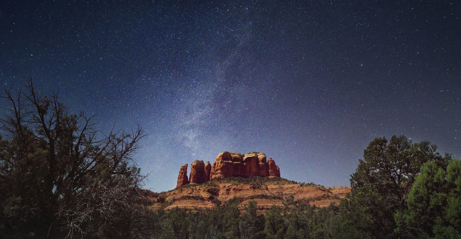 4K Ultra HD desktop wallpaper of a starry dusk sky featuring the Milky Way above a rugged desert landscape with rock formations and sparse trees.