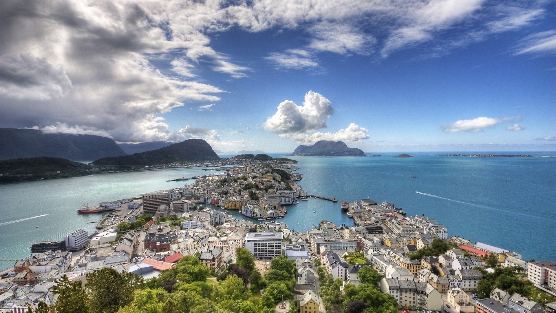 A panoramic HD view of Ålesund cityscape along Norway’s coastline, showcasing the ocean, man-made structures, and mountainous backdrop under a vibrant sky.