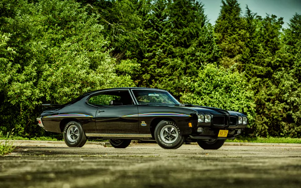 A sleek black Pontiac GTO muscle car parked against a backdrop of lush greenery, showcasing its classic design in vibrant 4K Ultra HD quality.