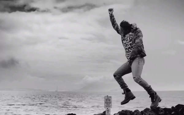 A monochrome HD wallpaper of a rapper jumping joyfully by the ocean, embodying the energy of music and the spirit of Kendrick Lamar.