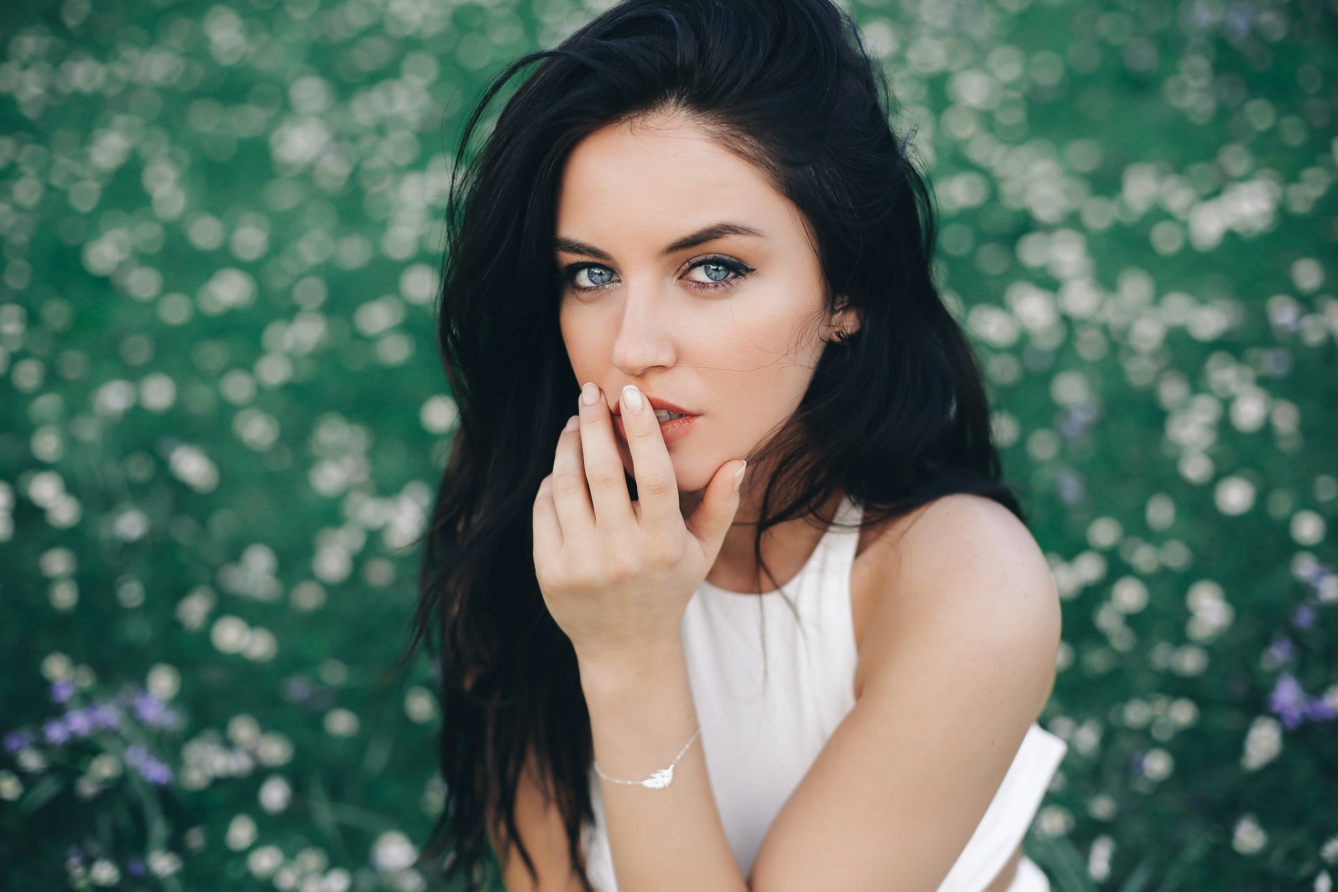A woman with blue eyes and black hair poses gracefully in a flower-filled meadow, wearing a striking dress. This HD image captures her beauty and serene expression.