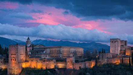 Alhambra fortress in Spain illuminated at sunset beneath dramatic clouds, captured in a vibrant HD desktop wallpaper background.