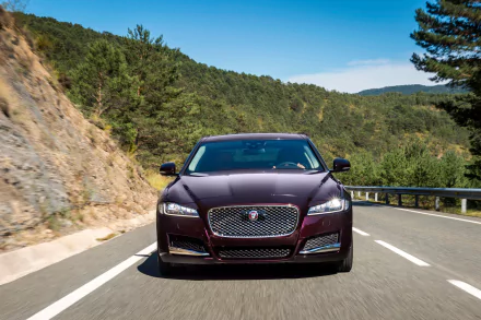 Front view of a maroon Jaguar XF car driving along a winding mountain road, vehicle captured in crisp detail — 4K Ultra HD PC desktop wallpaper background.