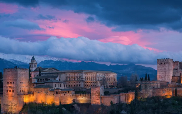 Alhambra fortress in Spain illuminated at sunset beneath dramatic clouds, captured in a vibrant HD desktop wallpaper background.