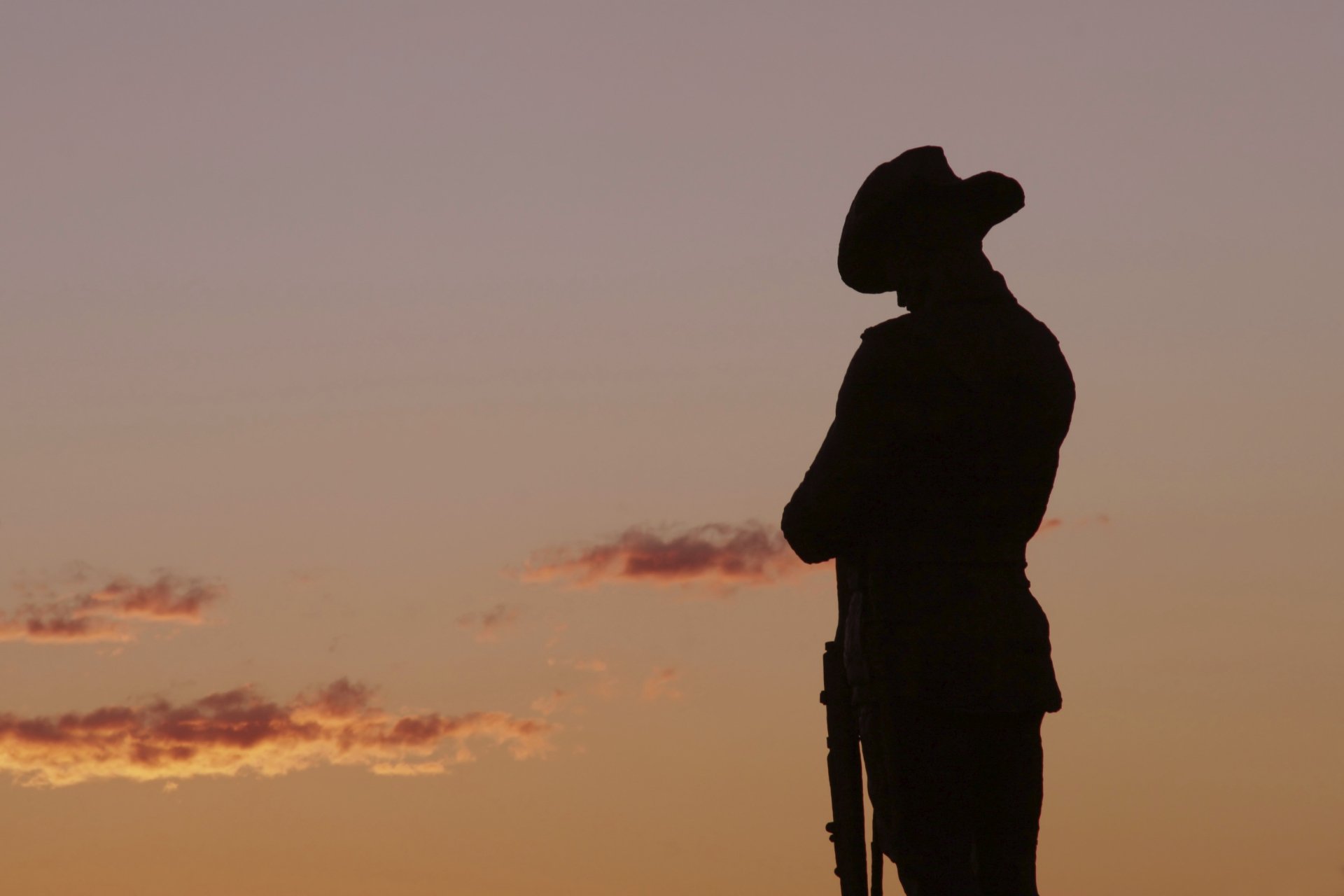 Silhouette of a soldier at sunrise honoring ANZAC Day against an orange sky — 2K Quad HD PC desktop wallpaper/background.