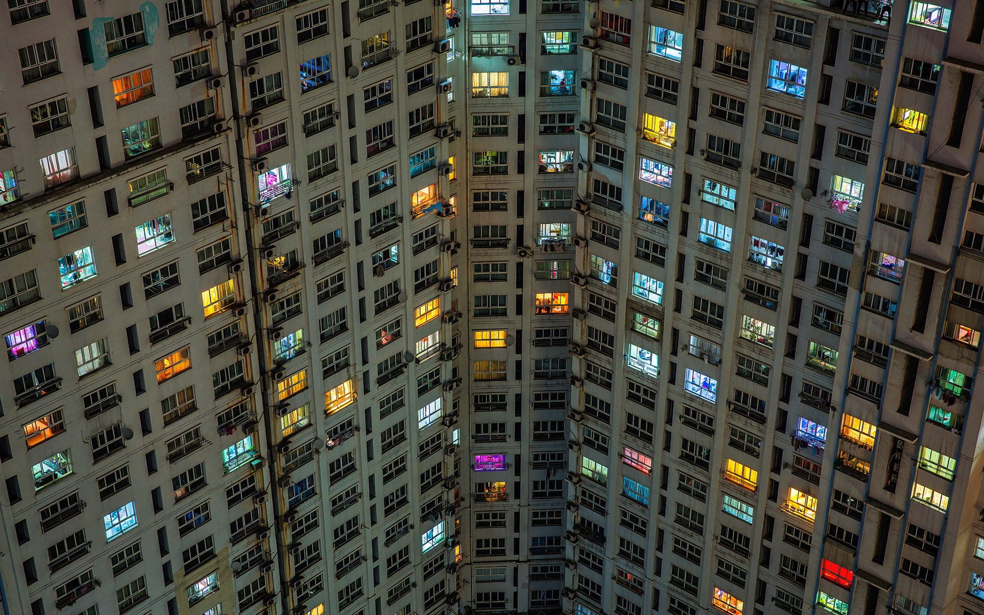 HD desktop wallpaper showing a colorful array of illuminated windows in a tall apartment skyscraper, highlighting vibrant man-made architectural patterns at night.