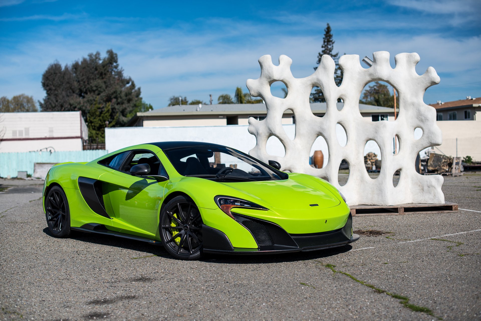 Bright green McLaren 675LT supercar parked outdoors with modern white sculpture and blue sky, captured as an HD PC desktop wallpaper and background.