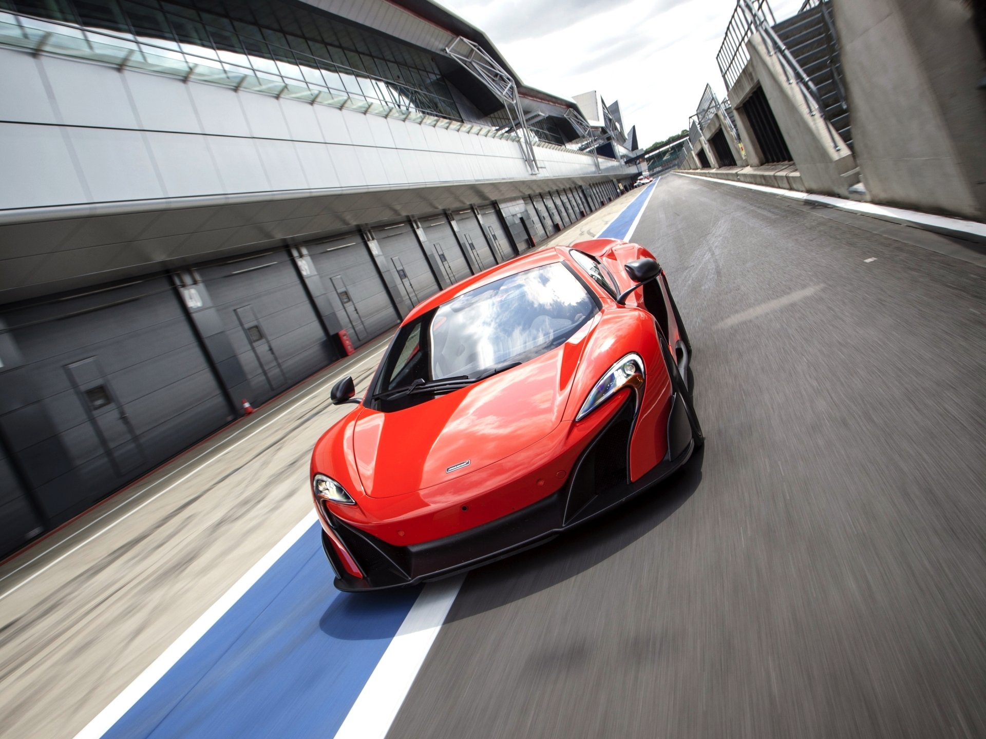 Front three-quarter view of a red McLaren 675LT supercar speeding down a racetrack pit lane — 2K Quad HD PC desktop wallpaper/background.