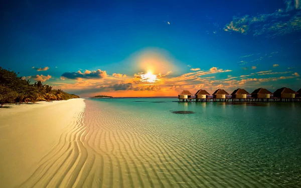 Sunset over a tropical beach with clear sand, ocean, and man-made bungalows extending into the water, captured in HD for a serene desktop wallpaper background.