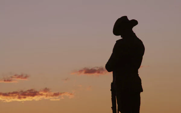 Silhouette of a soldier at sunrise honoring ANZAC Day against an orange sky — 2K Quad HD PC desktop wallpaper/background.
