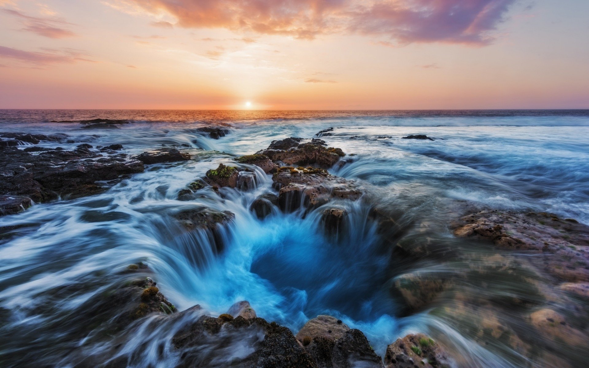 HD PC desktop wallpaper of Thor's Well: ocean waves rushing into a rocky sinkhole at sunset on the horizon, dramatic nature seascape.