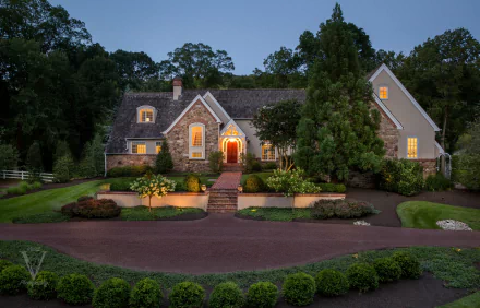 A beautifully illuminated stone house at dusk, surrounded by lush greenery and well-maintained landscaping, captured in stunning 4K Ultra HD.