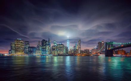 HD desktop wallpaper featuring the illuminated Brooklyn Bridge and New York City skyline at night, with city lights reflecting on the water under a dramatic sky.