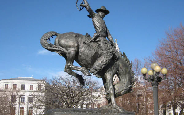 Metal cowboy statue on a bucking horse in downtown Denver, Colorado, USA, against a clear blue sky — 2K Quad HD PC desktop wallpaper/background.