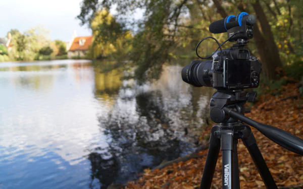 A Sony camera on a tripod, equipped with a microphone, overlooks a serene pond surrounded by trees. The image captures the tranquil beauty of the lake setting in stunning 4K Ultra HD.