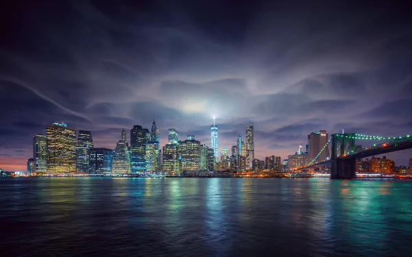 HD desktop wallpaper featuring the illuminated Brooklyn Bridge and New York City skyline at night, with city lights reflecting on the water under a dramatic sky.