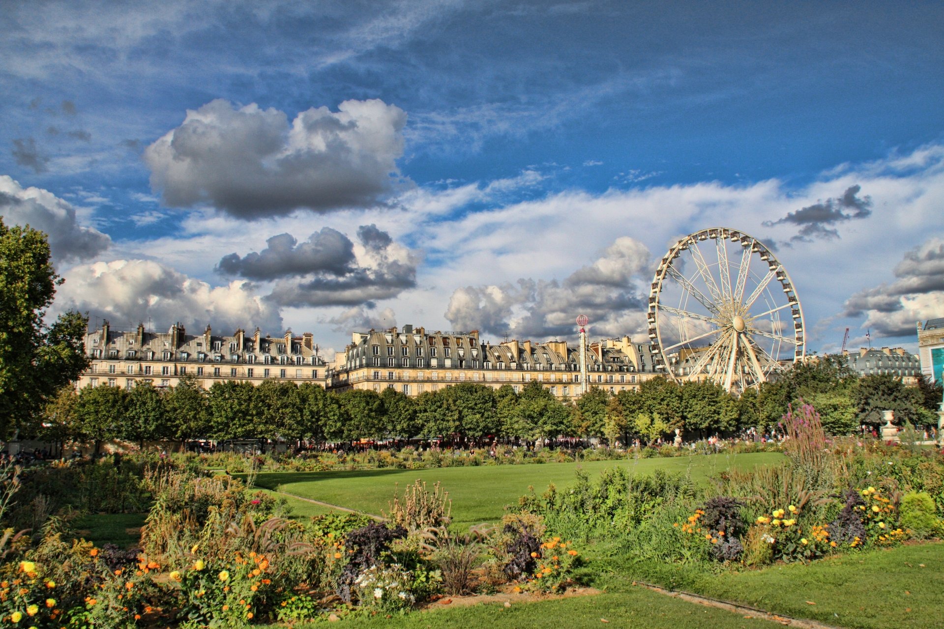4K Ultra HD PC desktop wallpaper of a Paris garden with colorful flower beds and lawns, a man-made Ferris wheel rising above tree-lined avenues beneath a dramatic cloudy sky.