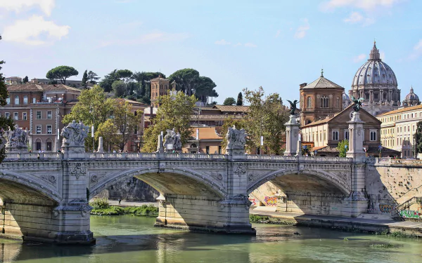 A stunning view of a historic bridge in Rome, Italy, showcasing intricate architecture against a serene river backdrop and the iconic dome of St. Peter’s Basilica in the distance.