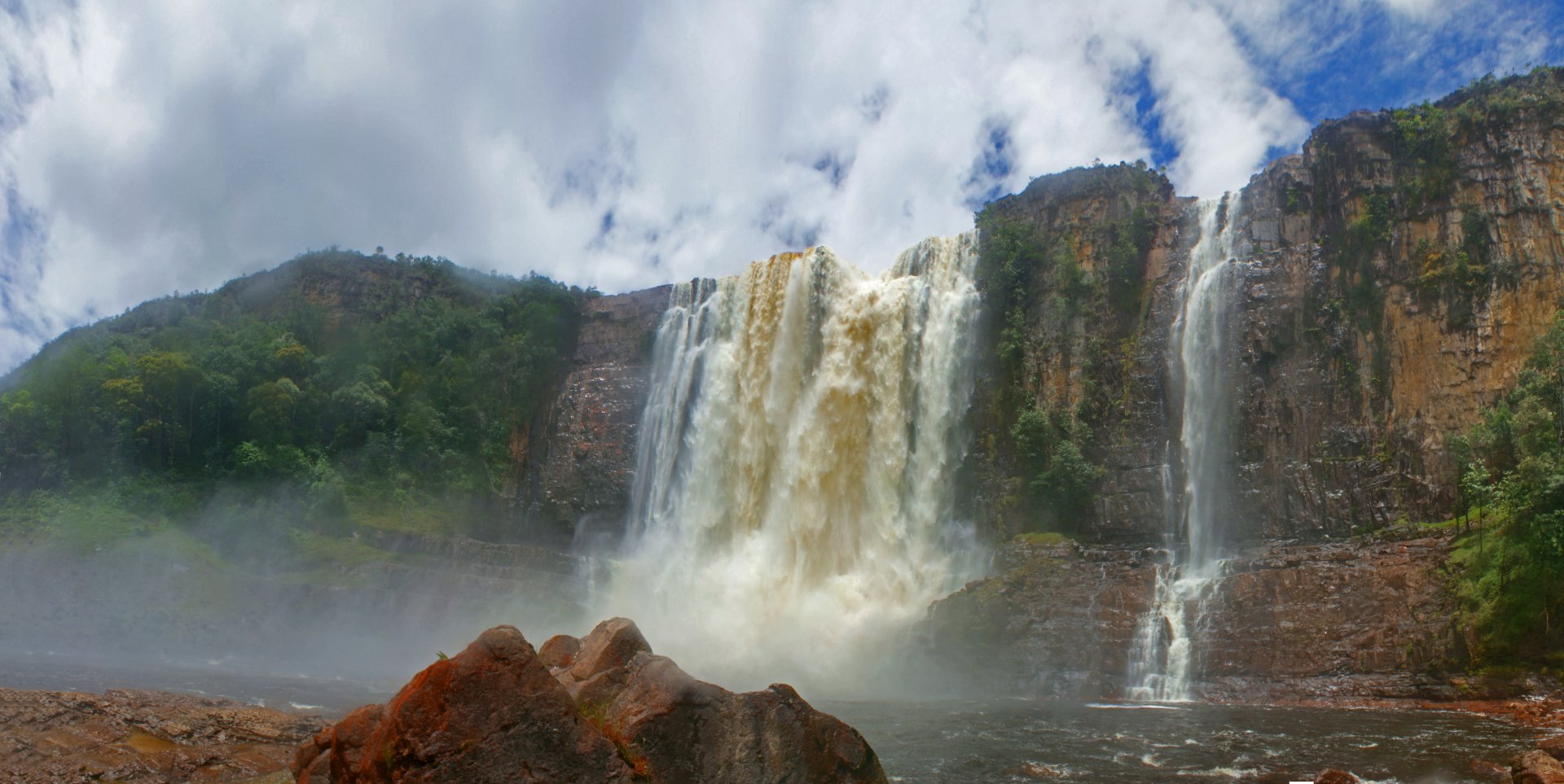 A stunning waterfall cascades over rocky cliffs in Guyana's lush mountains, surrounded by dense greenery and a misty atmosphere, creating a breathtaking nature scene.