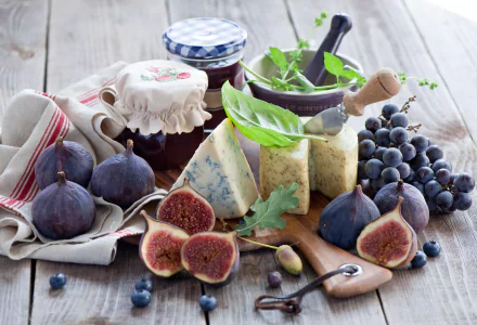 HD desktop wallpaper featuring a still life of fresh grapes, figs, assorted cheeses, and jars of jam on a rustic wooden table.
