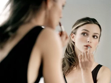 HD desktop wallpaper featuring Keira Knightley applying lipstick while looking into a mirror, set against a soft background.